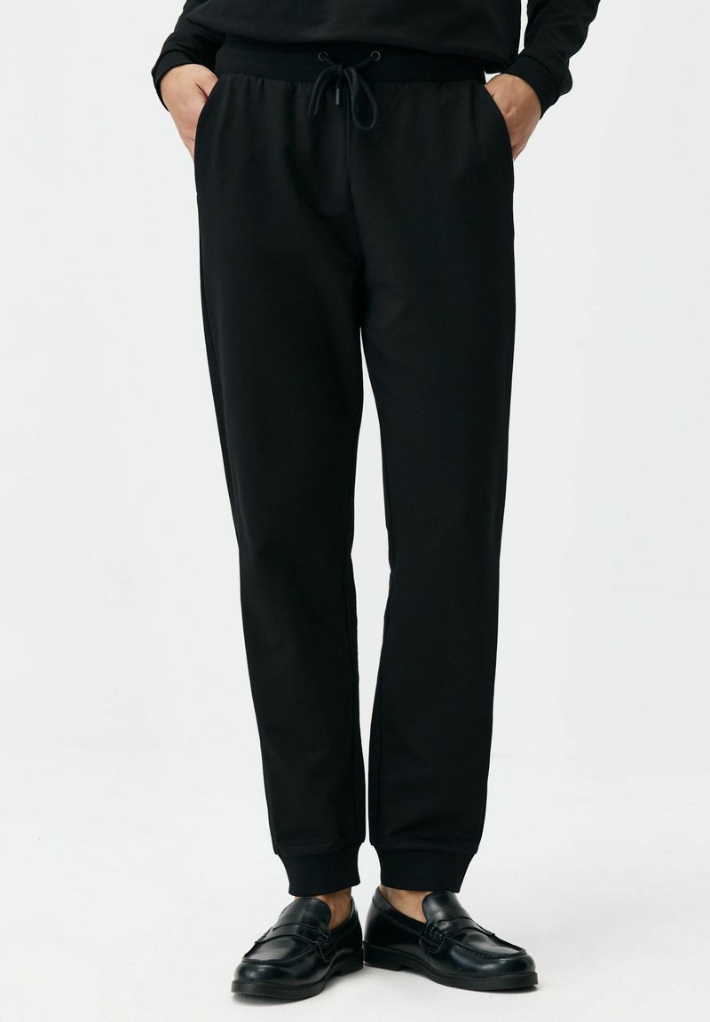 Czarne spodnie dresowe z regulowanym sznurkiem w talii, zwężanymi mankietami i bocznymi kieszeniami, wykonane z miękkiego, gładkiego materiału dla komfortu.