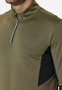Olivgrüner Pullover mit einem Halsreißverschluss, kontrastierenden schwarzen Seitenpaneelen und subtiler Textur. Mit "ENDURANCE"-Markenlogo auf der Brust.