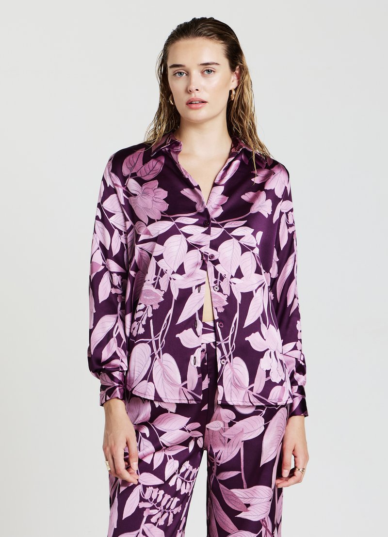 Blusa in satin a maniche lunghe di colore viola scuro con un motivo floreale rosa. Presenta un colletto e una chiusura con bottoni frontale, con una vestibilità rilassata.