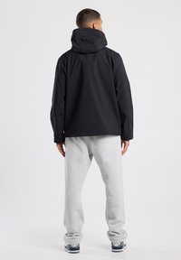 Black waterproof jacket with a hood, featuring side panels and a straight cut. Paired with gray sweatpants and sneakers.