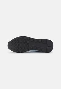 Black rubber shoe sole with textured grip pattern and raised rectangular studs, featuring a slight curve at the heel and toe area.