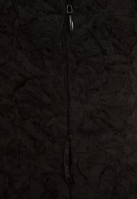 Tissu en dentelle noire avec des motifs floraux, comportant une fermeture éclair centrale noire avec une petite tirette, vue en gros plan.