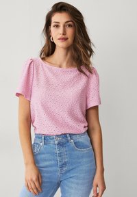 Rosa kortærmet bluse med hulmønster og afrundet halsudskæring, parret med lyseblå jeans med høj talje. Glat tekstur og afslappet pasform.