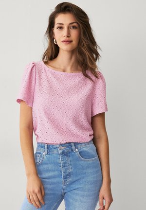 Top rosa de manga corta con patrón de ojales y escote redondeado, combinado con jeans de tiro alto en azul claro. Textura suave y corte relajado.