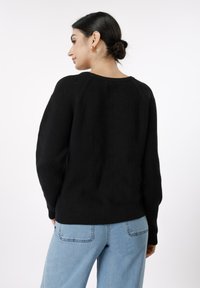 Μαύρο πλεκτό πουλόβερ με άνετη γραμμή, ριμπ υφή και ραγκλάν μανίκια. Συνδυάζεται με ανοιχτό μπλε τζιν τζιν, παρουσιάζοντας ένα casual στυλ.