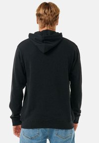Sudadera negra con bolsillo canguro y capucha. Presenta un dobladillo y puños de canalé, hecha de un tejido suave, combinada con jeans de color azul claro.