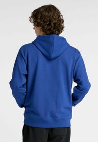 Felpa blu con cappuccio, maniche lunghe, polsini a coste e tasca a marsupio. Presenta un design minimalista e una texture morbida.