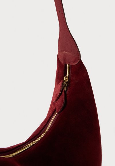 Burgundy suède schoudertas met een gouden rits, leren hengsel en een zachte textuur. Opvallende ritstrekkers en accentdetails op het ritsgebied.