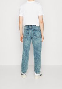 Jeans de mezclilla azul claro con un corte holgado, dos bolsillos traseros y un ligero desgaste. Combinados con zapatillas blancas y una camiseta blanca sencilla.