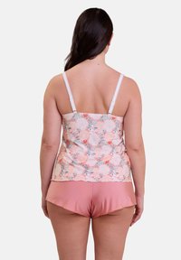 Camisole floral avec des bretelles en dentelle blanche, arborant un motif pêche et vert, associé à un short rose, texture lisse et coupe décontractée.