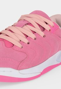 Κοντινό πλάνο ενός ροζ αθλητικού παπουτσιού με ανοιχτό ροζ κορδόνια, υφές σουέντ και δίχτυ, και λευκή σόλα με ροζ λεπτομέρεια.