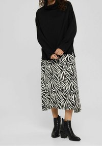 Zwart langwerpig top met kraag, gecombineerd met een middellange zebra-gepatroone rok in zwart en wit, en zwarte hoge enkellaarsjes.