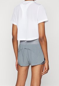 Camiseta corta de malla blanca con mangas cortas, combinada con pantalones cortos deportivos grises que presentan un dobladillo en capas y una cinturilla elástica.