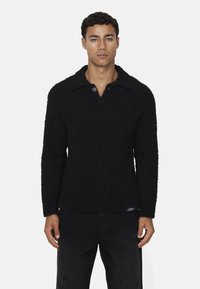Maglione nero a trama con colletto e patta a due bottoni, caratterizzato da maniche lunghe e una vestibilità rilassata. Abbinato a jeans scuri.