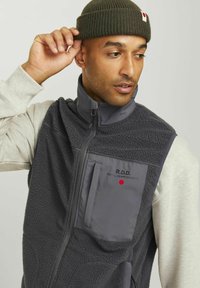 Mannen mouwloze vest in donkergrijze fleece met een ritssluiting aan de voorkant, hoge kraag en borstzak met het "R.D.D." logo en rode stipdetail.