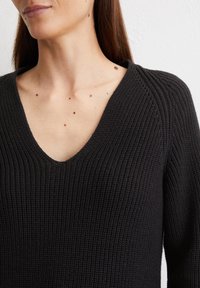 Schwarzer, gestrickter Pullover mit tiefem V-Ausschnitt, gerippter Textur und dezent strukturiertem Stoff. Enganliegendes Design, das Ausschnitt und Schultern betont.