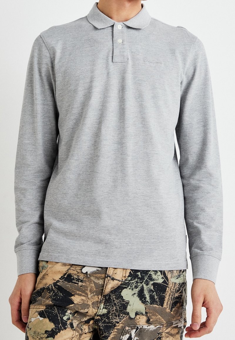 Harmaa pitkähihainen polo paita pehmeästä puuvillasekoitteesta, jossa on klassinen kaulus ja kolme nappia, yhdistettynä camo-kuosisin housuihin.