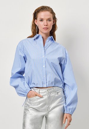 Blauw-wit gestreepte button-up shirt met een cropped ontwerp, poflange mouwen en een verstelbare zoom, gecombineerd met glanzende zilveren broeken.
