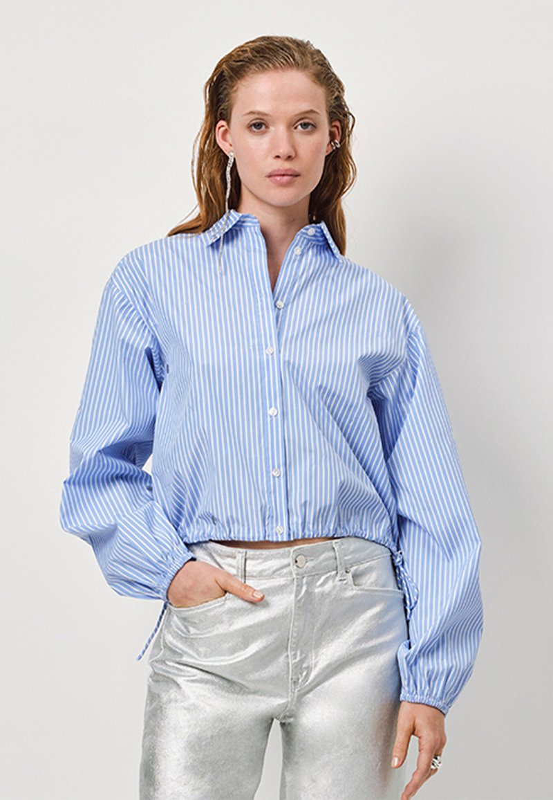 Blauw-wit gestreepte button-up shirt met een cropped ontwerp, poflange mouwen en een verstelbare zoom, gecombineerd met glanzende zilveren broeken.