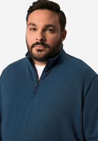 Námořnický zipový pulovr vyrobený z měkké, pružné látky. Obsahuje stojáček a krátký zip. Hladký povrch bez vzorů.