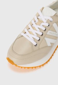 Baskets beiges avec des accents blancs, tige en cuir lisse, bout rond, lacets blancs, œillets en métal argenté, semelle en caoutchouc orange avec un motif de semelle.