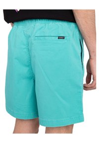 Shorts de bain turquoise en tissu léger, dotés d'une taille élastique, de poches latérales et d'une poche plaquée au dos avec un logo.