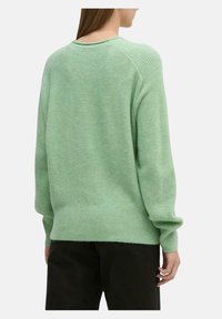 Maglione verde a maglia con una vestibilità comoda, dettagli a coste sulle spalle e un ampio polsino. Texture liscia con scollo rotondo e colore uniforme.