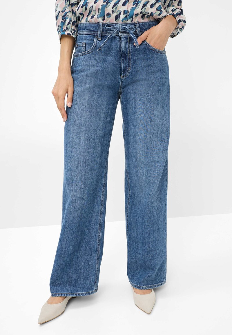 Wide-leg blue denim jeans with a high waist, front pockets, and a relaxed fit. Paired with beige pointed-toe heels.