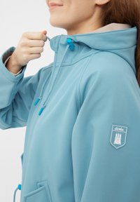 Giacca impermeabile blu con cappuccio, dotata di cordini regolabili, due tasche frontali e una toppa con logo sulla manica. Texture liscia.
