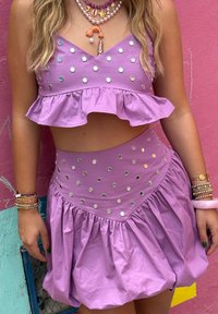 Ensemble deux pièces en tissu violet clair avec des bords volants. Présente des accents circulaires métalliques et un design de jupe évasée.