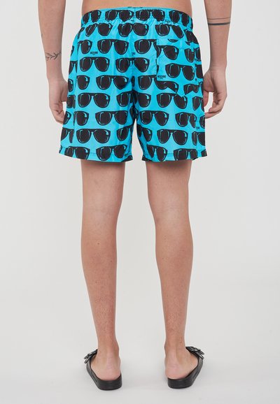 Costumi da bagno blu chiaro con un motivo ripetuto di occhiali da sole neri. Vita elastica con tasca posteriore. Texture del tessuto liscia.