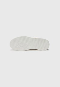 Sola de sapato branca de borracha com padrões de textura para aderência, featuring uma impressão de logotipo circular e ranhuras horizontais para tração.