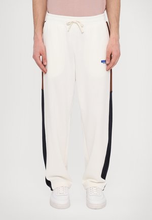 White sweatpants with black and brown side panels, elastic waistband with a drawstring, featuring a small blue logo on the left leg.