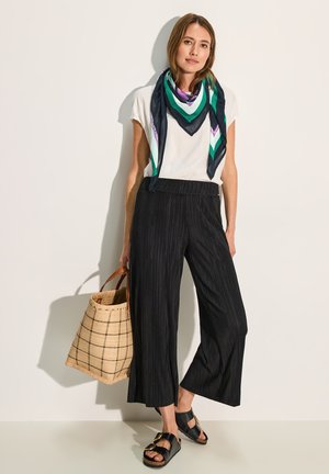 Camicia bianca a maniche corte, culotte nere a righe, sciarpa multicolore, sandali neri e borsa intrecciata color sabbia con motivo a griglia.