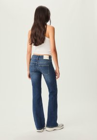 Dzwony niebieskie dżinsy z jasnym praniem i pięcioma kieszeniami, z subtelnymi detalami przeszycia oraz markowym paskiem widok z tyłu.