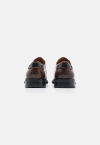 Scarpe di pelle con una combinazione di colori marrone e nero, caratterizzate da una superficie liscia, forma arrotondata e robuste suole in gomma nera.