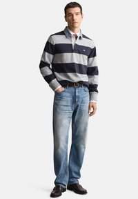 Ilgas rankovėmis polo marškinėliai tamsiai mėlynos ir pilkos dryžuotos spalvos, su apykakle ir kišene, derinami su šviesiai mėlynais džinsais ir tamsiais batais.