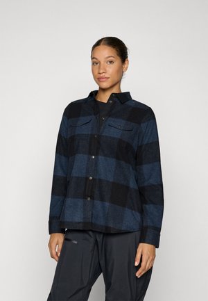 Button-up flannel shirt in navy and black check pattern, two chest pockets, and collar. Fabric appears soft and slightly textured.