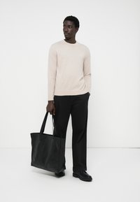 Un suéter de punto beige claro, pantalones negros y un bolso de cuero negro con asas de hombro, con un fondo blanco liso.