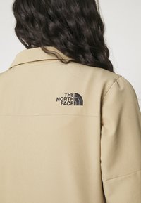 Beige kavaj med krage i mjukt tyg som har "The North Face"-logotypen i svart på högra sidan. Skräddarsydd passform med avslappnade ärmar.