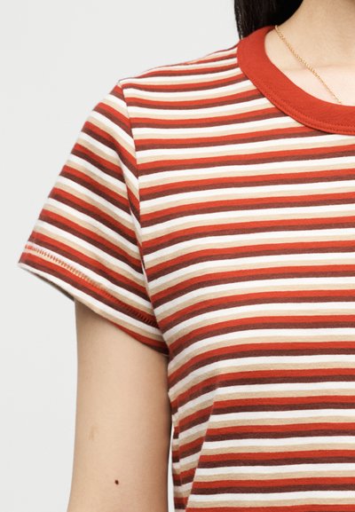 Κοντινό πλάνο ατόμου που φορά κοντομάνικο μπλουζάκι με οριζόντιες ρίγες σε κόκκινους, πορτοκαλί, καφέ και κρεμ τόνους με κόκκινο γιακά.