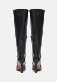 Schwarze Lederkniehohe Stiefel mit einem eleganten Design, spitzer Toes und hohen Stiletto-Absätzen; mit Reißverschlussakzenten auf der Rückseite.