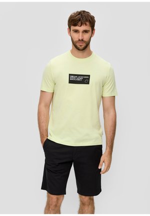 T-shirt jaune clair à manches courtes, avec un graphique rectangulaire noir comportant du texte blanc. Associé à un short noir.