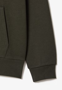Détail de manche et de poche de sweat-shirt vert foncé, montrant un poignet côtelé et une couture latérale.