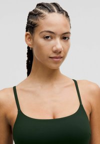 Top sin mangas de color verde oscuro con tirantes finos. Tela suave y diseño minimalista, con un escote cuadrado y una silueta ajustada.