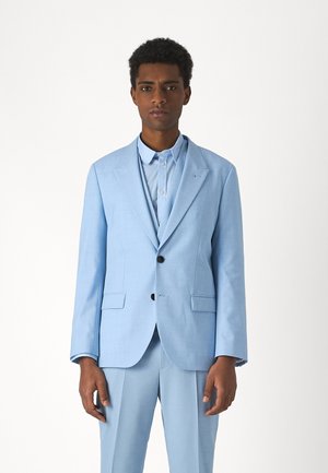 Completo azzurro chiaro con una vestibilità su misura, caratterizzato da una giacca monopetto, rever a taglio e due bottoni. Indossato sopra una camicia coordinata.