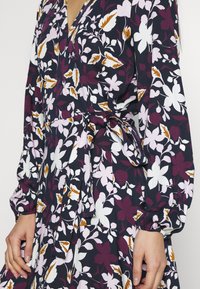 Šaty s květinovým potiskem v námořnické modři se růžovými, bílými a burgundskými květinami. Mají dlouhé rukávy, výstřih do V a pásek v pase pro zvýraznění postavy. Hladká tkanina.