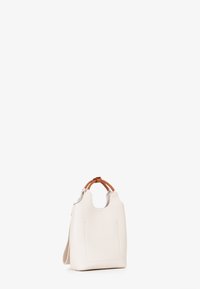 Borsa in pelle bianca testurizzata con manici curvi marroni e una tracolla removibile, in piedi su uno sfondo chiaro e semplice.