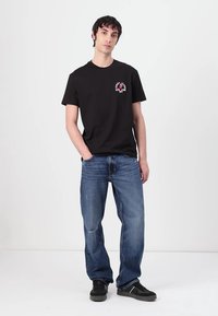Black cotton t-shirt with a front graphic design, paired with blue denim jeans. The jeans have a relaxed fit and faded patches. Black sneakers worn.