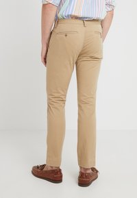 Lichtbruine chinos met achterzakken, slim fit, platte voorkant en subtiele textuur, gecombineerd met bruine bootschoenen.